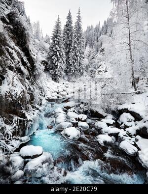 Splendido paesaggio di fiume d'acqua blu e foresta di alberi di abete rosso in montagna con neve in inverno Foto Stock