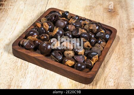 Guarana (Paullinia Cupolana) semi in una ciotola piatta di legno su un taglio di legno Foto Stock