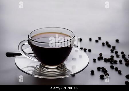 Caffè nero in una tazza trasparente e chicchi di caffè il tavolo Foto Stock
