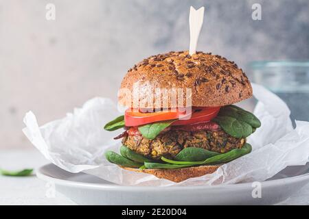 Hamburger di lenticchie vegane con patate dolci al forno, salsa di pomodoro e verdure fresche su un piatto grigio. Concetto di cibo vegano. Foto Stock