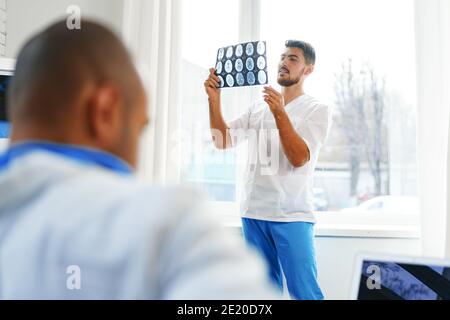 Due medici di sesso maschile esaminano la risonanza magnetica cerebrale di un paziente nel cabinet Foto Stock