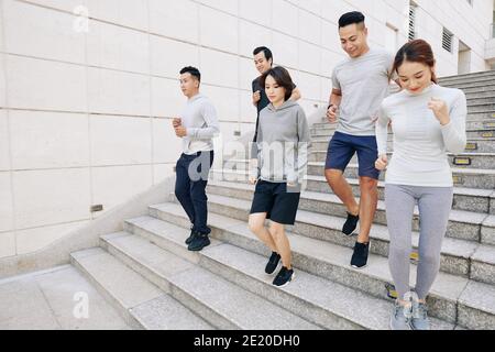 Adatta giovani uomini e donne asiatici che corrono giù le scale in città quando si allenano per la maratona al mattino Foto Stock