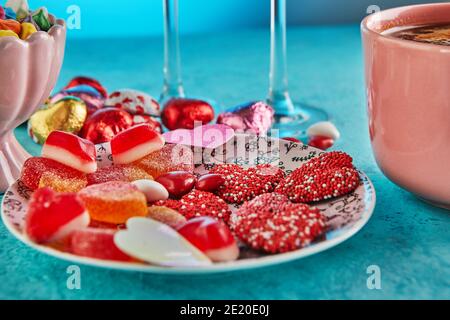 San Valentino o cena romantica con cuori di caramelle, una tazza di caffè caldo e tavolo elegante su uno sfondo azzurro Foto Stock