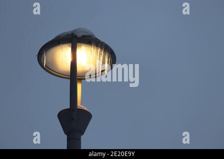 Lampada a LED incandescente coperta di icicles su sfondo del cielo invernale. Illuminazione elettrica, lanterna a risparmio energetico Foto Stock