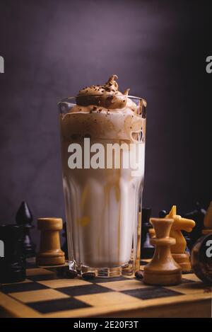 Caffè Dalgona. Bevanda ghiacciata montata con caffè istantaneo popolare in Corea cocktail cremoso in bicchieri alti decorati con scacchi su scacchiera di legno Foto Stock