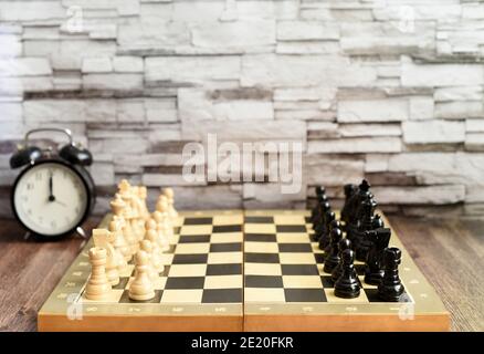 Pezzi di scacchi sulla scacchiera e sveglia sul tavolo di legno. Sfondo sfocato con spazio di copia Foto Stock