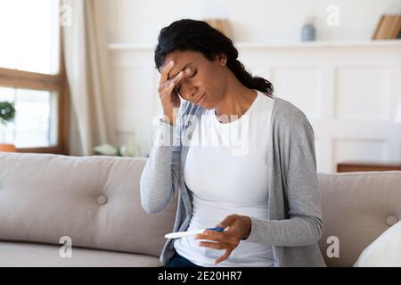 Frustrata giovane donna afroamericana che guarda al test di gravidanza. Foto Stock