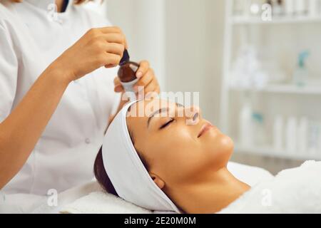 Mani di terapeuta pronte a mettere l'olio nutriente della pelle a. i giovani donne si affrontano durante la procedura di skincare Foto Stock