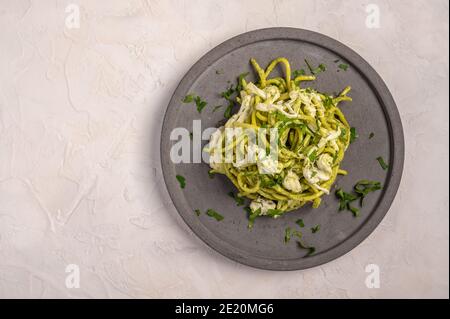 Primo piano pasta con pesto, stracciatella e prezzemolo servita su piatto grigio in ceramica su sfondo chiaro, fuoco selettivo, vista dall'alto, spazio copia Foto Stock