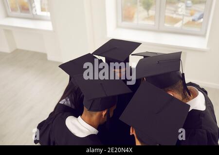 Gruppo di laureati in caps quadrati che si avvicinano in cerchio, abbracciandosi l'un l'altro Foto Stock