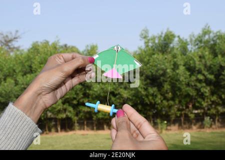 Femmina, donna, ragazza che vola un kite giocattolo in miniatura con la bobina giocattolo in miniatura manjha nel parco. In occasione di kite festa di volo di uttarayan, makars Foto Stock