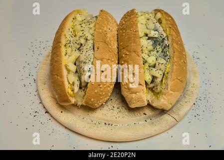 Due deliziosi panini tradizionali con aringhe di Amsterdam con involtini di semi di sesamo, senape gialla, crauti e cipolla bianca su un piatto rotondo di legno Foto Stock