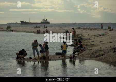 Le persone che hanno attività ricreative sulla spiaggia di Cilincing, sulla zona costiera di Jakarta, Indonesia, dove il traffico del porto di Jakarta può essere visto in lontananza. Foto Stock