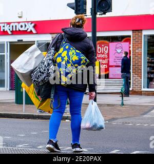 London UK, Woman Alone porta borse per lo shopping in attesa di attraversare la strada a High Street Traffic Lights Foto Stock