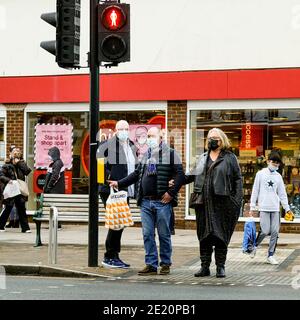 Londra UK, Senior Couple che indossa una copertura protettiva per il viso in attesa di attraversare la strada al Traffic Lights Carriing Shopping Foto Stock