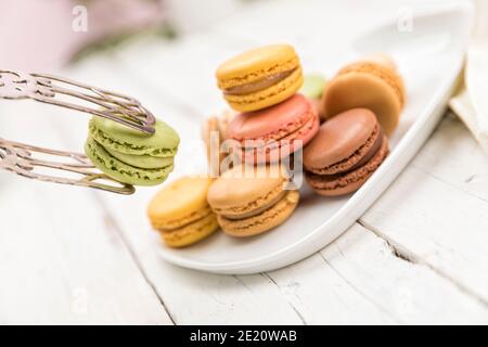 Prendendo un macaron al pistacchio con pinze per pasticceria da un assortimento su un piatto, vista inclinata Foto Stock