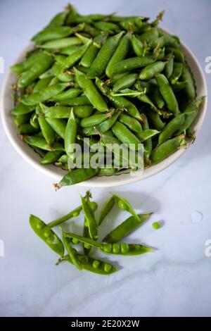 Piselli. Cialde di piselli verdi in un piatto su un tavolo bianco. Vendemmia. Primo piano su cibo sano. Spazio di copia Foto Stock