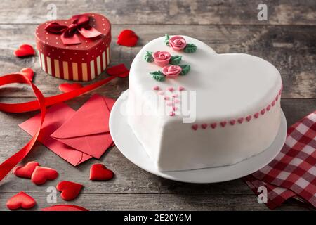 Torta cuore per San Valentino, Festa della mamma o compleanno, decorata con rose e cuori di zucchero rosa su tavola di legno Foto Stock