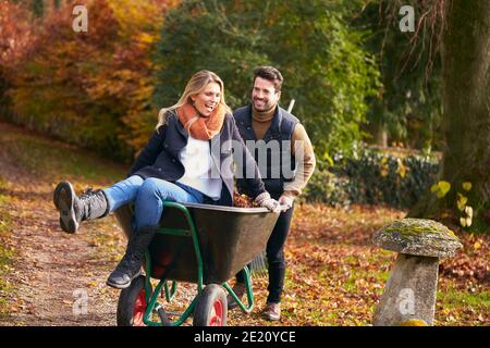 Uomo che spinge la donna in Wheelbarrow come coppia Rake Autunno foglie Dal giardino insieme Foto Stock