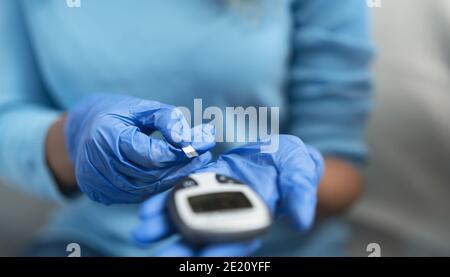 Giovane infermiera che controlla il test della glicemia per il diabete mentre indossa un chirurgico Guanti - concetto sanitario - Focus morbido sui guanti Foto Stock