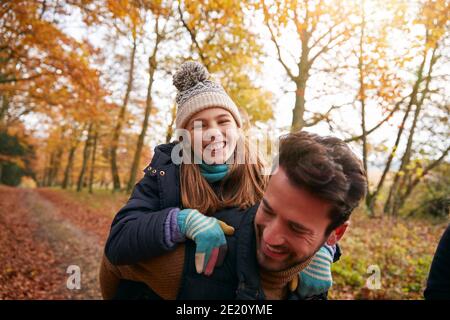 Padre che dà figlia di Laughing Piggyback giro in famiglia passeggiata attraverso Bosco d'autunno Foto Stock
