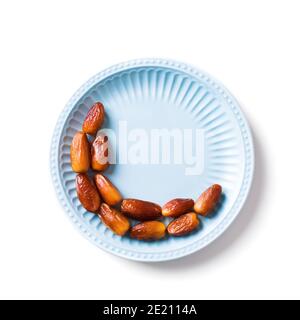 Mezzaluna islamica. Ramadan kareem con frutta datteri disposti a forma di luna crescente su piatto blu isolato su sfondo bianco, vista dall'alto, spazio copia Foto Stock