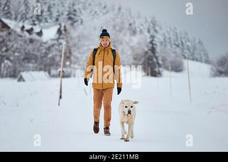 Vista frontale del giovane con il cane in inverno. Proprietario di animali domestici con il suo labrador che riever camminando contro la natura bella durante la nevica. Montagne di Jizera, C. Foto Stock