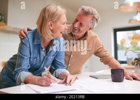 Coppia matura che esamina e firma finanze nazionali e documenti di investimento In cucina a casa Foto Stock