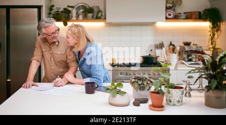 Coppia matura che esamina e firma finanze nazionali e documenti di investimento In cucina a casa Foto Stock