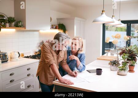 Coppia matura che esamina e firma finanze nazionali e documenti di investimento In cucina a casa Foto Stock