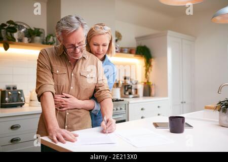 Coppia matura che esamina e firma finanze nazionali e documenti di investimento In cucina a casa Foto Stock