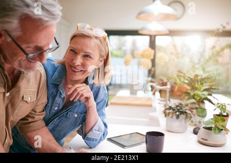 Coppia matura che esamina e firma finanze nazionali e documenti di investimento In cucina a casa Foto Stock