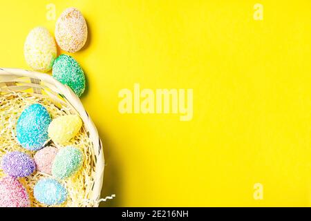 Buona Pasqua. Uova pastello in cestino su sfondo giallo piatto con spazio per il testo. Foto Stock