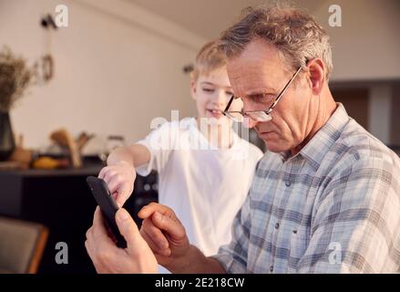 Nipote mostrando nonno come risolvere il problema e utilizzare Mobile Telefono a casa Foto Stock