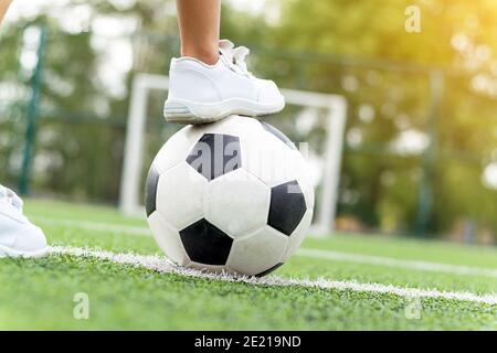 Piedi di un ragazzo che indossa sneakers bianche che salpano su una palla di calcio nel mezzo del campo di calcio. Foto Stock