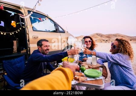 Gruppo di amici caucasici adulti si divertono e festeggiano insieme in amicizia all'aperto con tavolo e cibo e furgone veicolo intorno - allegro e t Foto Stock