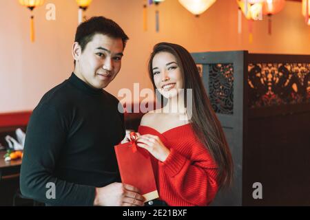 Bella giovane coppia asiatica in abiti rossi dare presente in Festoso cinese vietnamita ristorante colorato lanterne di carta che celebra cinese nuovo Anno Foto Stock