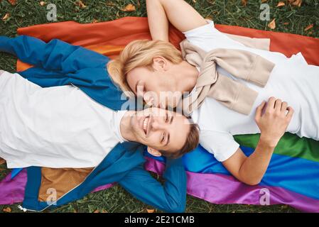 Coppia gay amorevole che ha date romantiche all'aperto. Due bei uomini che giacciono insieme sulla bandiera dell'orgoglio di LGBT. Foto Stock