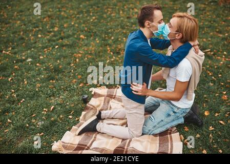 Romantica coppia gay all'aperto. Amore durante il coronavirus. Due bei uomini che si baciano indossando maschere per il viso. Protezione Covid-19. Foto Stock