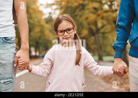 Immagine ritagliata di due genitori gay con la loro figlia adottiva che tiene le mani e cammina nel parco insieme. Buon concetto di famiglia LGBT. Foto Stock