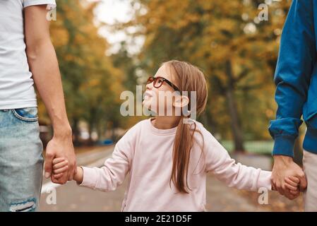 Immagine ritagliata di due genitori gay con la loro figlia adottiva che tiene le mani e cammina nel parco insieme. Buon concetto di famiglia LGBT. Foto Stock