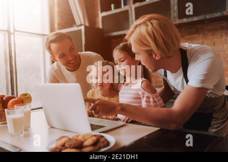 Coppia gay con le loro figlie adorabili che leggono la ricetta sul computer portatile e cucinando in cucina. Famiglia LGBT a casa. Foto Stock