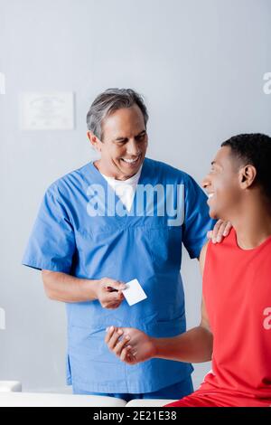 felice medico che dà la carta bianca a allegro sportivo afroamericano Foto Stock