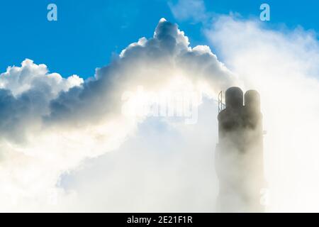 Camino di fumo industriale che mette fuori vapore e fumo su un cielo blu chiaro. Foto Stock