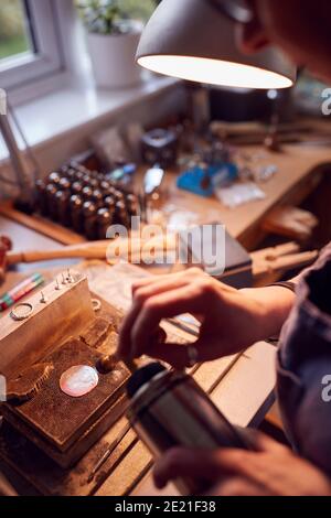 Primo piano di Jeweler maschio che lavora su Brooch con Blowcannello In Studio Foto Stock