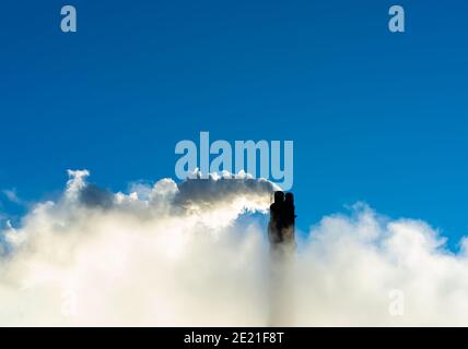 Camino di fumo industriale che mette fuori vapore e fumo su un cielo blu chiaro. Foto Stock