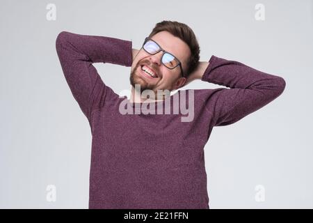 Giovane bell'uomo con barba che indossa un maglione casual e occhiali che rilassano e stretching, braccia e mani dietro la testa e il collo sorridenti felici Foto Stock