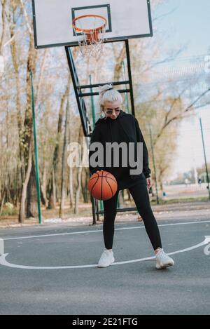 Lunghezza completa di bella donna che indossa bicchieri giocando a basket su campo all'aperto Foto Stock
