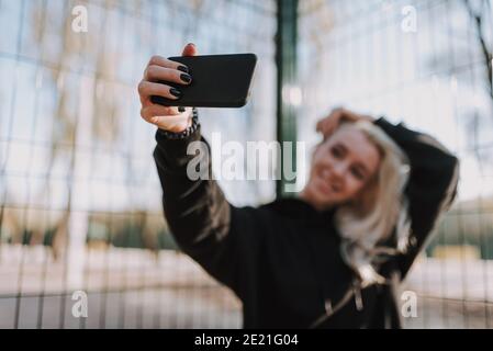 Felice donna divertente che fa selfie mentre tiene lo smartphone con il metallo griglia sullo sfondo Foto Stock