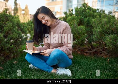 Adorabile giovane donna che ama un romanzo emozionante e trascorrere del tempo con esso all'aperto su un prato verde erba Foto Stock